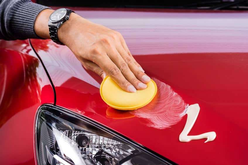 Here's an image of a man waxing a red car by hand.