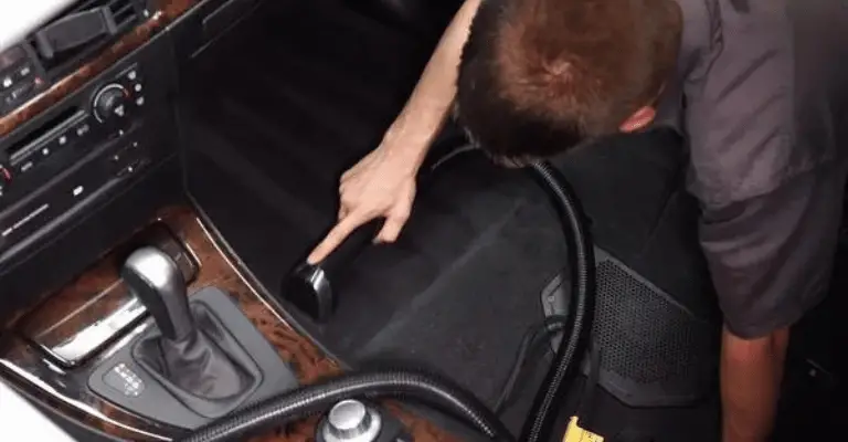 professional detailer vacuuming the black carpet inside a car