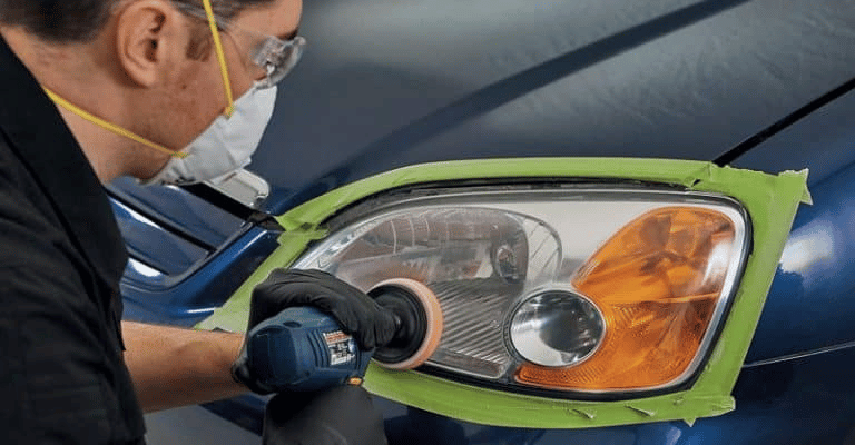 professional detailer that has masked off the headlight to restore it using a buffer