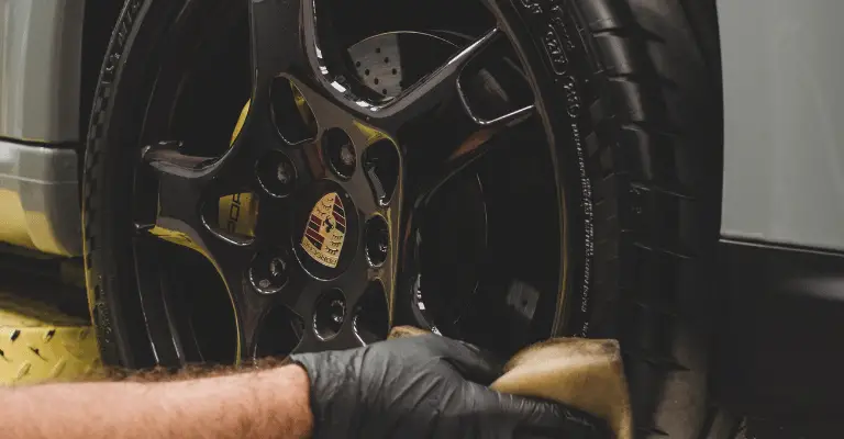 black porsche wheel having tire shine applied to the tire while it's on a yellow lift