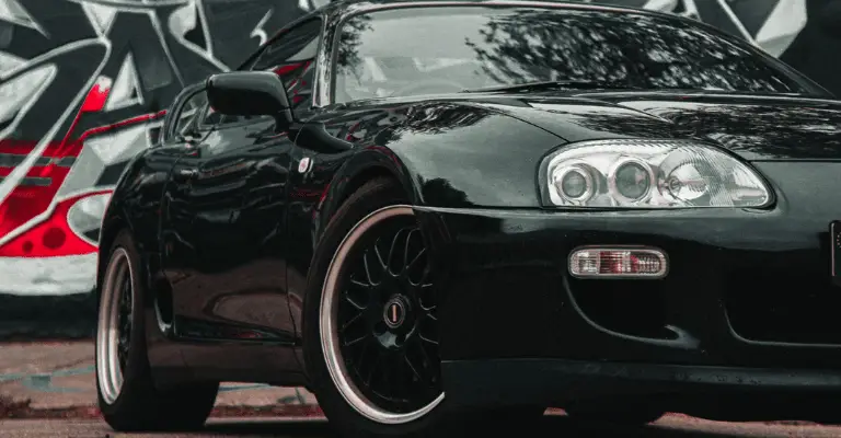 black toyota supra with a fresh coat of wax posed against a graffiti wall