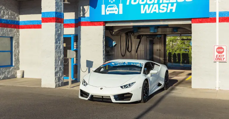 This is a picture of a white Lamborghini leaving a touchless car wash. This image is used to illustrate that a touchless car wash can be used safely, but does present hazards if used improperly.
